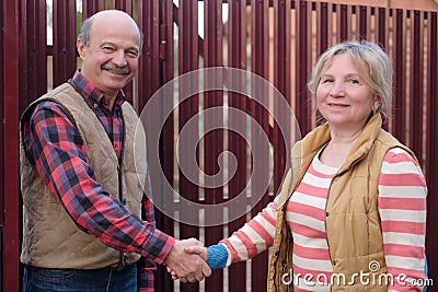 Two senior neighbors takling to each other on sunny day near fence Stock Photo