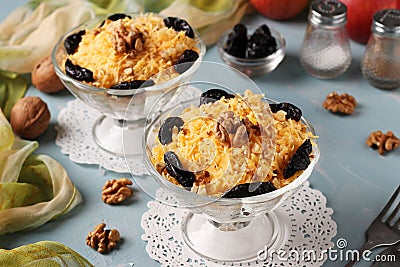 Two servings of salad with chicken, cheese and apples, decorated prunes and walnuts in glass bowls on light blue background, Stock Photo