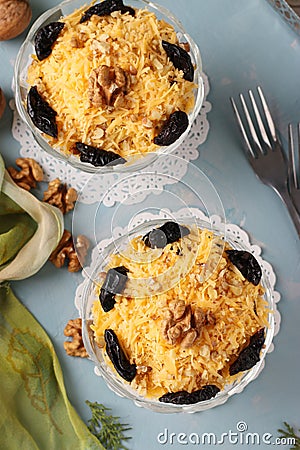 Two servings of salad with chicken, cheese and apples, decorated prunes and walnuts in glass bowls on light blue background Stock Photo