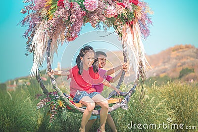 Two siblings children is swinging on a flower swing in a nature field for relaxation and childhood hapiness concept Stock Photo