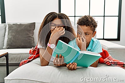 Two siblings lying on the sofa reading a book smelling something stinky and disgusting, intolerable smell, holding breath with Stock Photo