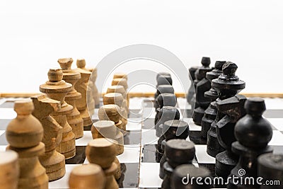 Two sides of black and white chess pieces, which are made of wood, are facing each other. There is a white background for placing Stock Photo