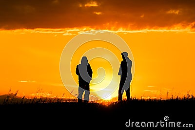 Two silhouettes of men talking at sunset or sunrise with dramatic sky and clouds.Dialogue and meeting two people on the horizon Stock Photo