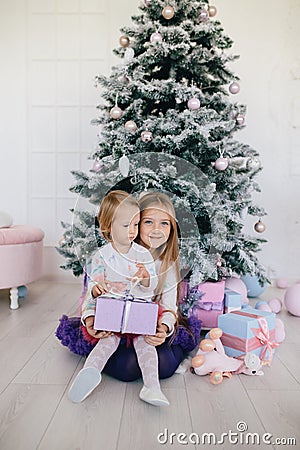 Two sisters at home with Christmas tree and presents. Happy children girls with Christmas gift boxes and decorations. Stock Photo