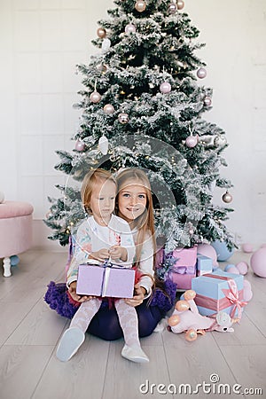 Two sisters at home with Christmas tree and presents. Happy children girls with Christmas gift boxes and decorations. Stock Photo
