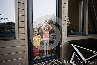 Two sisters looks throw the glass door on terrace of wooden country tiny cabin house Stock Photo