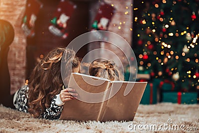 Two sisters holding a box with a gift in a green package. Christmas mood. In the background there is a decorated Christmas tree Stock Photo