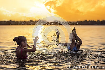 Two sisters splashing water playing in the lake at sunset background Stock Photo