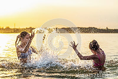 Two sisters splashing water playing in the lake at sunset background Stock Photo