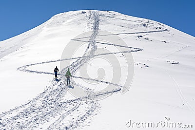 Two skiers come up the slope to the top. One goes on foot with skis fastened to a backpack, while the other goes skiing. Editorial Stock Photo