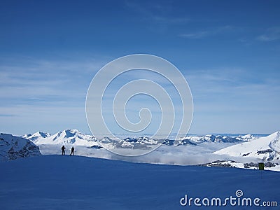 Two skiers in front of a cliff on a mountainside over the clouds in the French Alps. Stock Photo