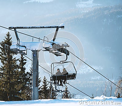 Two skiers riding a cable chair lift at a ski resort on a sunny day Editorial Stock Photo