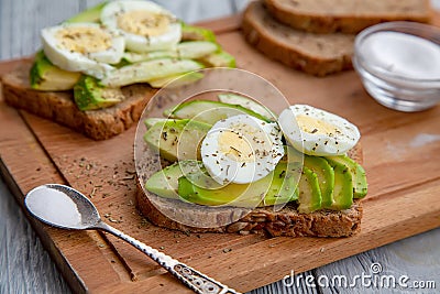 two sliced ripe avocado sandwiches with egg and spices on a wooden Board. Top view. Healthy breakfast Stock Photo