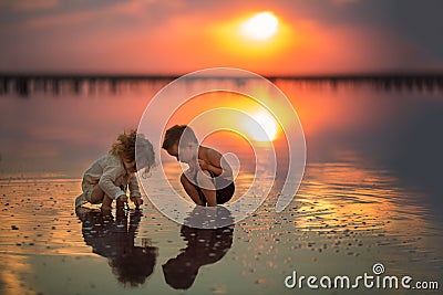 Two small children playing on the seashore during sunset Stock Photo