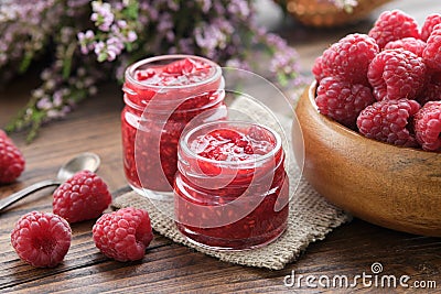 Two jars of raspberries jam, wooden bowl of fresh red raspberries on kitchen table Stock Photo