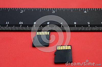 Two small micro SD memory cards lie on a red background next to a black ruler. A small and compact data and information store Stock Photo