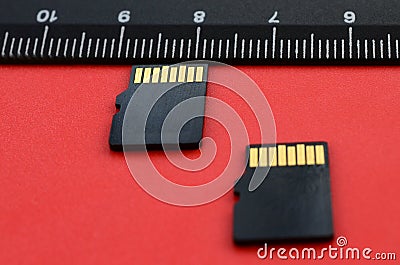 Two small micro SD memory cards lie on a red background next to a black ruler. A small and compact data and information store Stock Photo