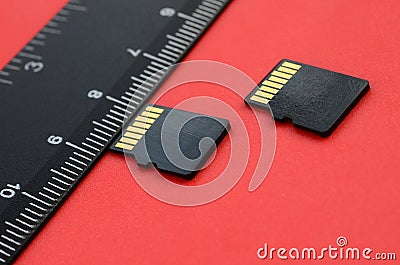 Two small micro SD memory cards lie on a red background next to a black ruler. A small and compact data and information store Stock Photo