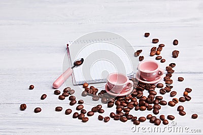 Two small pink cups on the table with a spoon, notepad and scattered coffee beans on a white wooden background. Stock Photo