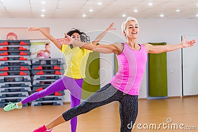 Two smiling athletic women doing aerobic dancing exercises holding their arms sideward indoors in fitness center. Stock Photo