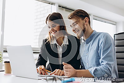 Two smiling businesspeople sitting together at a table in a modern office talking and using a laptop Stock Photo