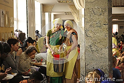 Two smiling female kitchen workers give to parishioners Prasad - food that is a religious offering in Krishnaism Editorial Stock Photo