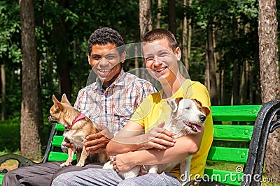 Two smiling friends with dogs relaxed on the bench in park in summer Stock Photo