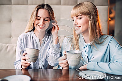 Two smiling girlfriends drinks coffee in cafe Stock Photo