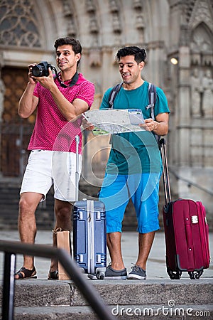Two smiling male tourists are walking with map and photographing Stock Photo