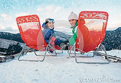 Two smiling skiers sit in chaise-longue on the mountain top Stock Photo