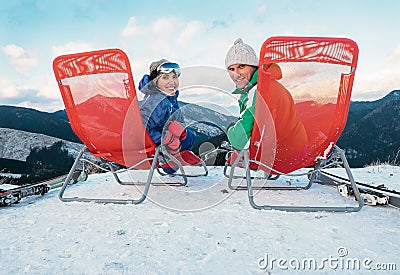 Two smiling skiers sit in chaise-longue on the mountain top Stock Photo