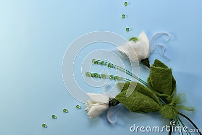 Two snowdrops made of wool in the lower right corner with wire beadwork on a blue sky background with green beads Stock Photo