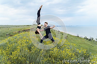 Two sportsmen practicing acro yoga together outdoors in the evening. Balancing girl legs up. Perfect flexibility. Athlete standing Stock Photo