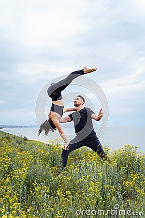 Two sportsmen practicing acro yoga together outdoors in the evening. Balancing girl legs up. Perfect flexibility. Athlete standing Stock Photo
