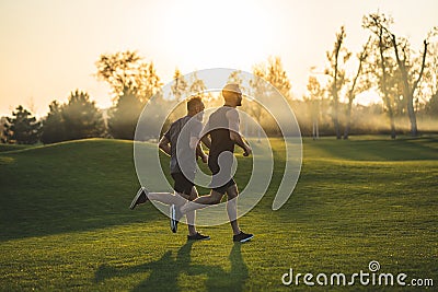 The two sportsmen running on the grass in the park on the sunny background. Stock Photo