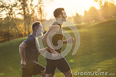 The two sportsmen running on the grass on the sunny background. Stock Photo