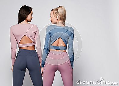 Two sporty blonde and brunette girls in athletic body cloth sport wear cloth stand together after workout on gray Stock Photo