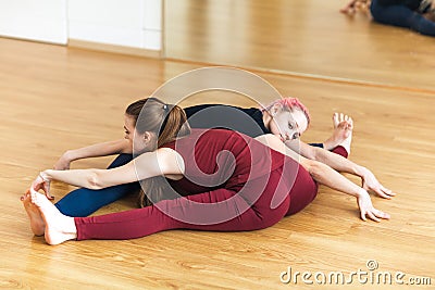 Two sporty girls in gym doing acroyoga, yoga with partner, Wide-Angle Seated Forward Bend, Upavishtha Konasana. Stock Photo