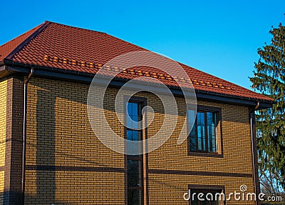Two-storey house with tall vertical window on the stairwell and show-guard on the metal tiled roof Stock Photo