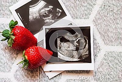 Two strawberry and a photo of a human fetus from an ultrasound scan during pregnancy on a gray background Stock Photo