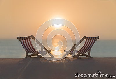 Two striped red-white sunbeds at sandy tropical sunset ocean beach. Stock Photo