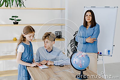 Two students are working on a project at school in a spacious classroom. The teacher observes the students` learning process. Stock Photo