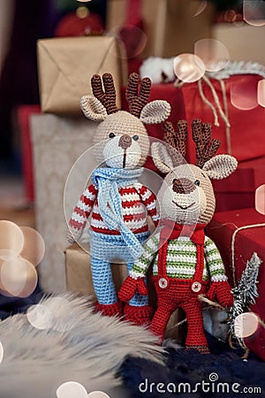 Two stylish amigurumi deers in striped sweaters, scarf and butterfly tie stands near Christmas presents Stock Photo