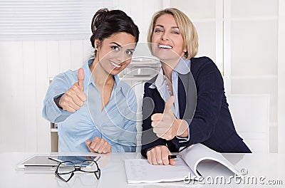 Two successful business women with thumbs up at office. Stock Photo