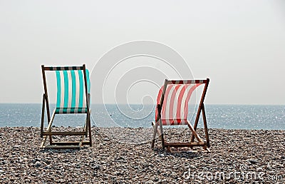 Two sunlit deckchairs on a pebble beach Stock Photo
