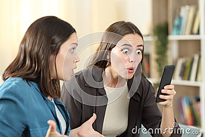 Two surprised friends checking smart phone content Stock Photo