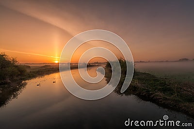 Two swans drifting along a misty river Nene at sunrise Stock Photo