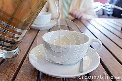 Two teacups and French press on the table, blurred woman behind. Pouring tea concept. Stock Photo