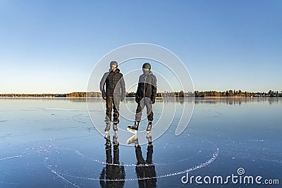 Two teenage boys are posing for memory photo before ice skating - on the crystal clear frozen lake. The big frozen lake in Stock Photo