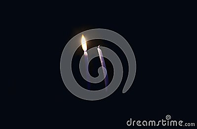 Two thin candles, one is on, the other is off. A burning candle illuminates the second candle. Stock Photo